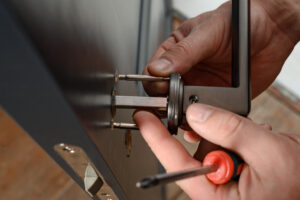 A Man Installs A Doorknob In A Door, Carpentry At Home.